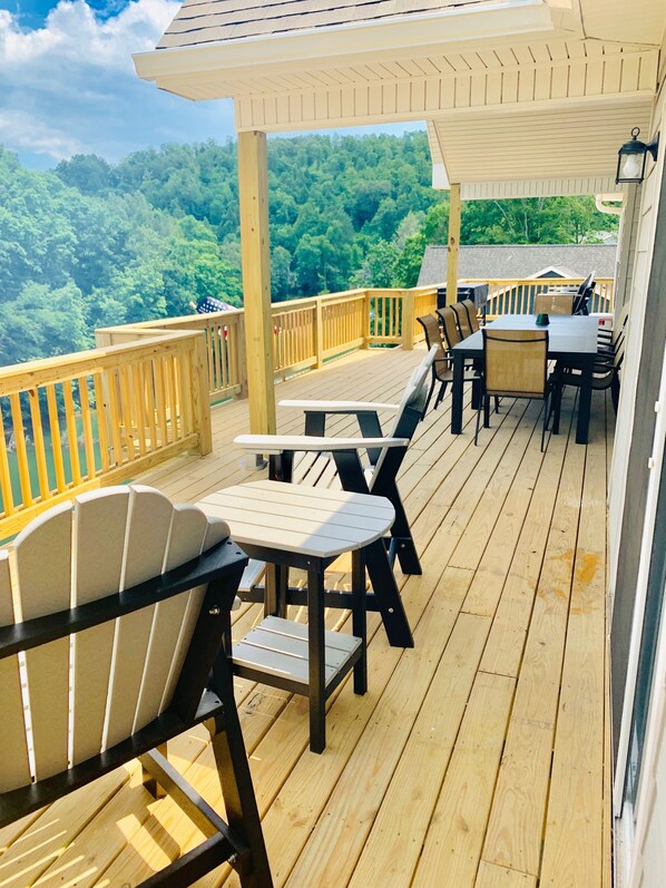 A wooden deck with outdoor furniture, including chairs and a table, overlooking a forested area.