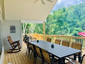 A covered deck with a table and chairs, a rocking chair, and a sign listing lake activities. - Norris Nook: Lakefront 9br/11ba, Private Dock,Private HotTub,Sleeps 32, Gameroom (LaFollette)