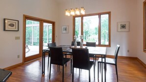 Un comedor con una mesa y sillas de madera, ventanas amplias y una lámpara colgante.