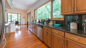 Cocina moderna con armarios de madera, encimera negra y ventanas amplias con vistas a zonas verdes.