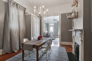 Uma sala de jantar com uma mesa de madeira, cadeiras e um candelabro. Há uma lareira com parapeito e esculturas de animais fixadas na parede.
