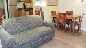 A living room with a patterned sofa, wooden dining table with chairs, and a kitchen area with cabinets and appliances. - 1 Bedroom Studio on the Virginia Beach waterfront (Virginia Beach)