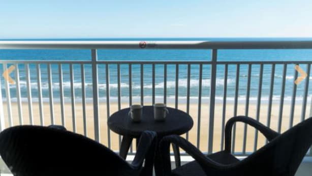 A balcony with a view of the ocean, a table with two cups, and a chair. - 1 Bedroom Studio on the Virginia Beach waterfront (Virginia Beach)