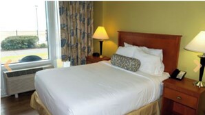 A hotel room with a large bed, a bedside table with a lamp, and a window with curtains. - 1 Bedroom Studio on the Virginia Beach waterfront (Virginia Beach)