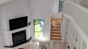 Een ruime woonkamer met een open haard, een grote flatscreen-tv, een bank en een trap naar een verdieping erboven.