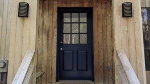 Een houten huis met een zwarte voordeur, een klein portaaltje en een raam boven de deur.