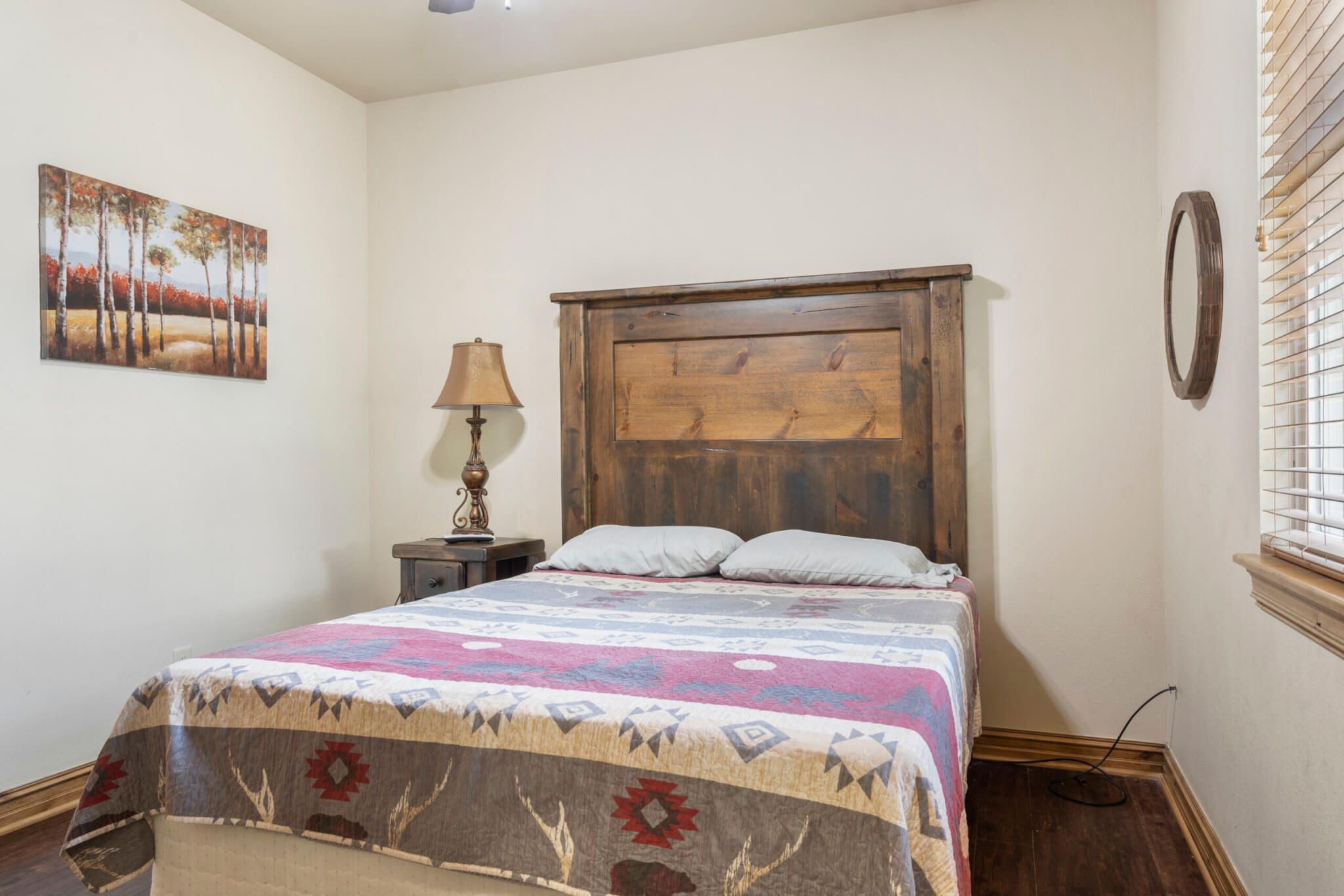 Une chambre à coucher avec une tête de lit en bois, une couvre-lit à motifs, une table de chevet avec une lampe et un tableau accroché au mur.