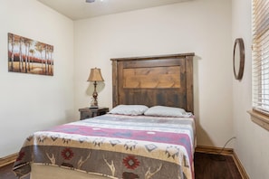 A bedroom with a wooden headboard, a patterned bedspread, a nightstand with a lamp, and a painting on the wall. - Lake View Retreat at CrossTimbers Marina (Sperry)
