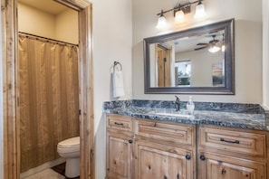 A bathroom with a shower, toilet, vanity with drawers, a mirror, and a ceiling fan.