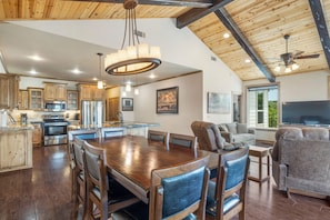 A spacious kitchen with wooden cabinets, a large dining table, and a ceiling fan.