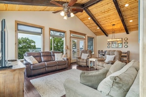 A spacious living room with a high ceiling, large windows, and a cozy seating area.