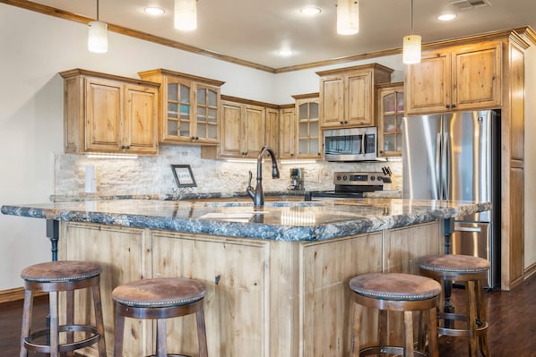 A kitchen with wooden cabinets, a granite countertop, a stainless steel refrigerator, and a built-in oven.