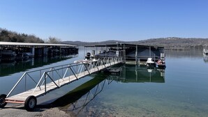 Un muelle con zona cubierta, embarcaciones y vistas despejadas del agua y colinas distantes.
