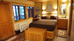 Ein gemütliches Schlafzimmer mit Bett, Nachttischen, einem kleinen Schreibtisch, einer Heizung und einem Fenster mit Blick auf Bäume.