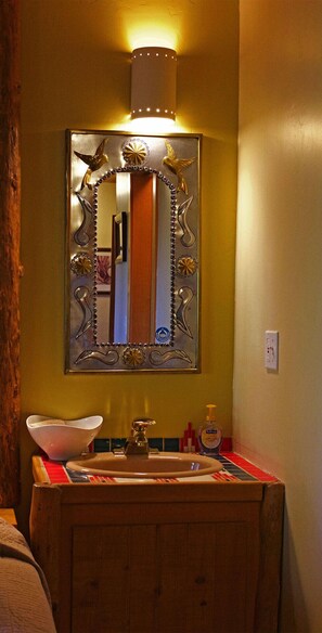 Een badkamer met een houten wastafelmeubel, een spiegel met decoratieve details en een wandlamp.