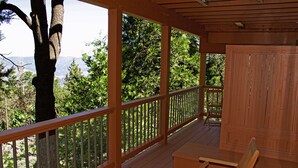 Eine Holzterrasse mit Bank und Tisch, mit Blick auf ein bewaldetes Gebiet und Berge in der Ferne.