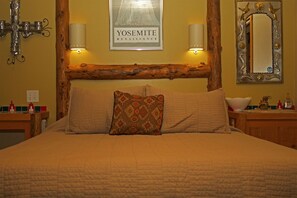 Een bed met een gewatteerde spreidekking, twee bedlampen, een lijst met daarin het kunstwerk “YOSSEMITE RENAISSANCE” en een houten hoofdbord.