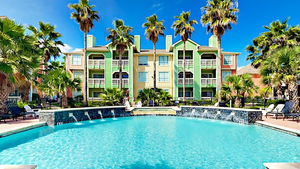 Un hotel con una piscina grande, varios balcones y palmeras.
