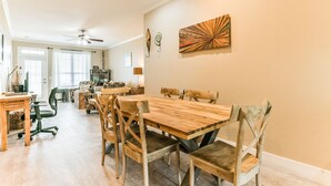 Un comedor con una mesa y sillas de madera, un ventilador de techo y obras de arte en la pared.