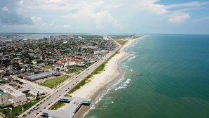 Vista aérea de una ciudad costera con una playa extensa, una carretera que bordea la costa y edificios a lo largo de la línea costera.