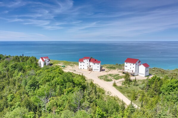 A coastal property with three white buildings with red roofs, surrounded by dense greenery and a clear view of the ocean.