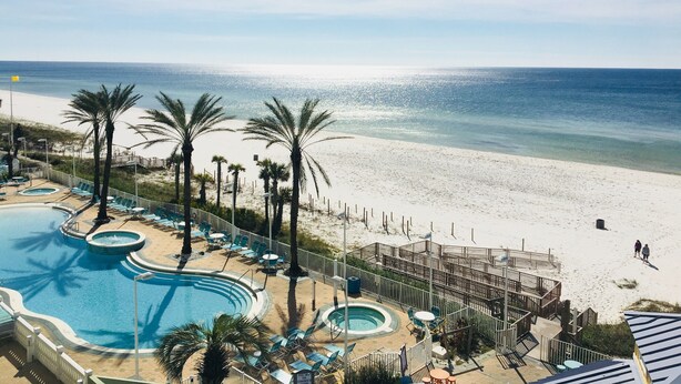Een resort met een zwembad, strand en palmbomen.