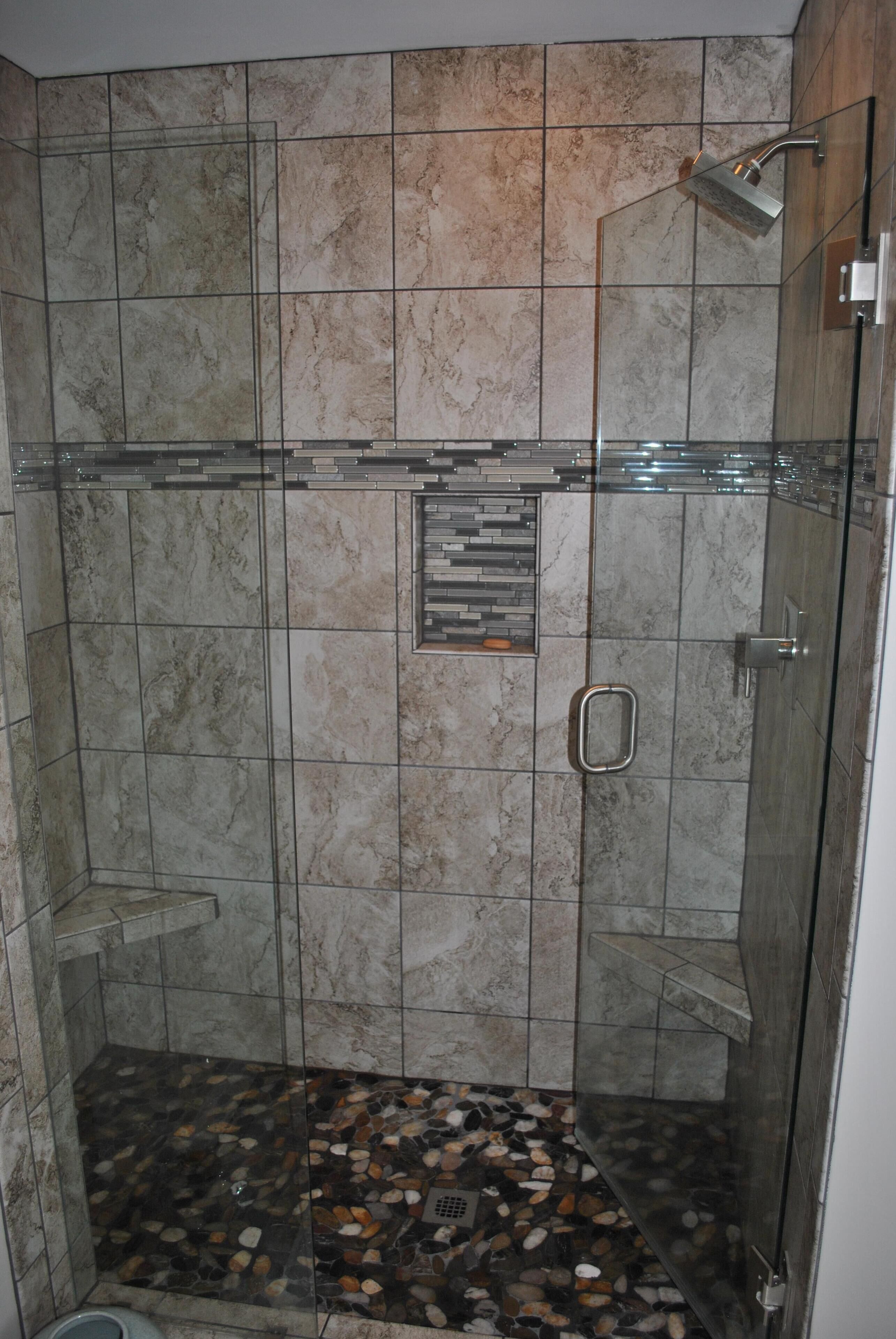Ducha con cerramiento de vidrio, piso con diseño de guijarros y jabonera empotrada.