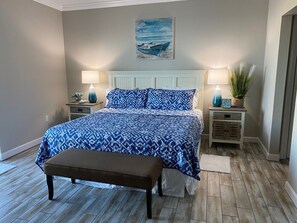 Ein Schlafzimmer mit einem Bett, zwei Nachttischen, einer Bank, einem Gemälde und einer Topfpflanze.