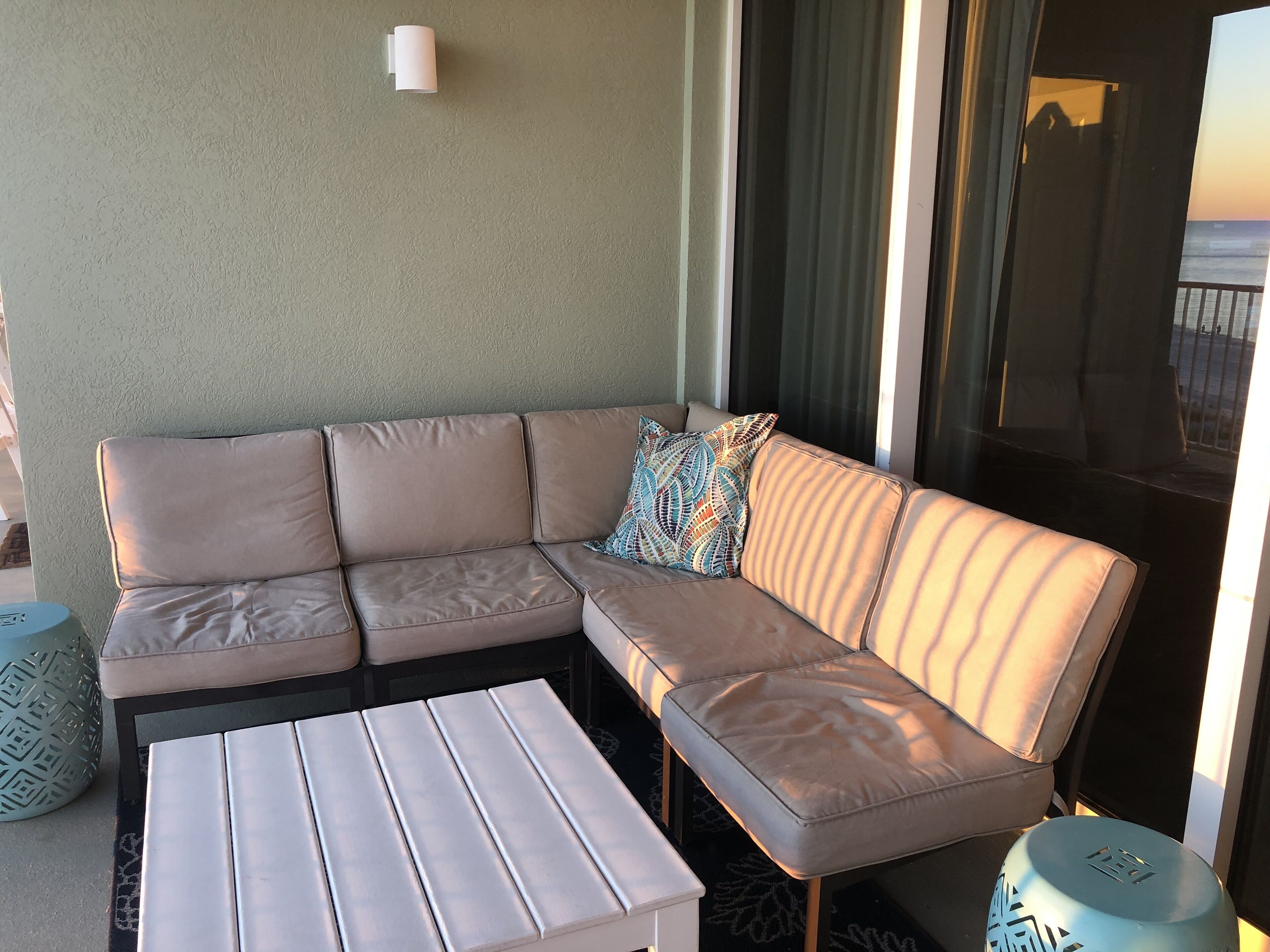 A beige sectional sofa with a patterned pillow, a white coffee table, and a patterned ottoman.