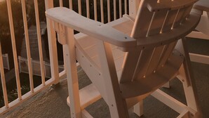 Een balkon met witte stoelen met uitzicht op een strand bij zonsondergang.