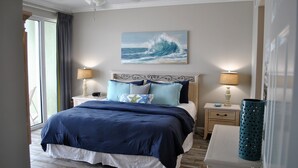 Een keurig opgemaakt slaapkamer met een bed, twee nachtkastjes, een lamp en een schilderij van een golf aan de muur.