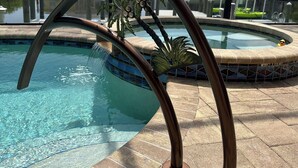 Uma área de piscina com água azul cristalina, um deck revestido de azulejos e uma vista de um edifício ao fundo.