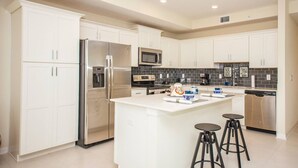 A modern kitchen with white cabinets, stainless steel appliances, a central island with stools, and a black tiled backsplash. - D-Gated Resort-5 miles to Disney-2 FREE Water Park (Osceola County)