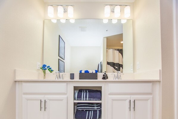 A bathroom with a large mirror, two sinks, a towel rack, and a shower curtain.