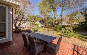 A patio with a brick floor, a dark table, wicker chairs, and a grill.