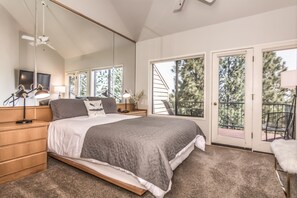 Relax in this serene bedroom with a large bed, nightstand, and mirror, plus a balcony with a tree-lined view.