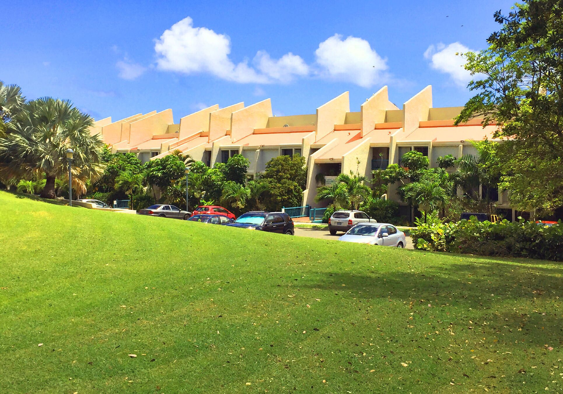 A hotel with multiple buildings, a parking lot, and a grassy area with trees.
