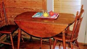 Une table de salle à manger en bois, avec des chaises, un plateau sur lequel se trouvent une théière, des tasses et une petite assiette.