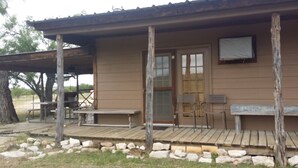 Une cabane rustique dotée d’une véranda, de fondations en pierre, ainsi que d’une table et de chaises en bois.