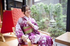 A person in traditional attire seated in a room with a view of a garden and a red structure.