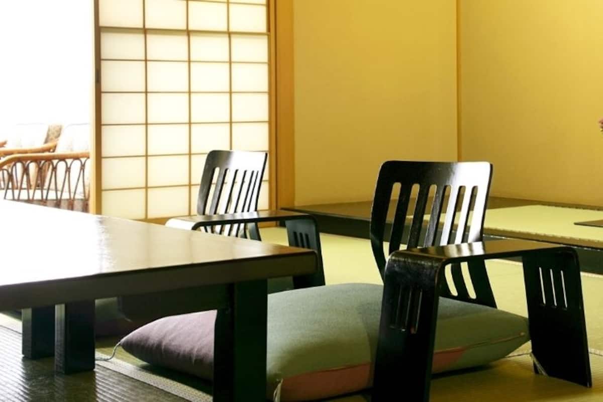 A traditional Japanese room with tatami flooring, a low table, and black chairs with cushions.