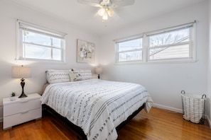 A bedroom with a bed, two bedside tables, a ceiling fan, and two windows.