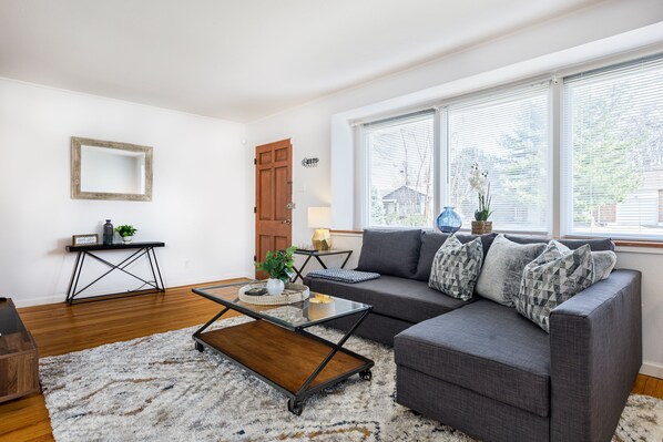 A living room with a gray sofa, a glass coffee table, a wooden side table, and a white rug. - Pretty *3BDR/2Bath Home* in a Good Area Next to Parks & Close to Downtown! (St. Louis)