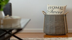 A framed abstract painting on a wall, a wicker basket with a pillow labeled "HOME Sweet Home" on a floor, and a chair with a plant. -  Pretty  *3BDR/2Bath Home* in a Good Area Next to Parks & Close to Downtown! (St. Louis)
