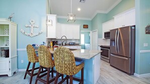 Una cocina con una isla central, armarios blancos, un refrigerador de acero inoxidable y una lámpara colgante.