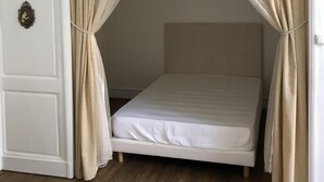 A single bed with a canopy, white walls, a wooden floor, and a wall-mounted light fixture. - Authentic 13th century chateau, in 3 acres  surrounded by high stone walls. (Limoges)