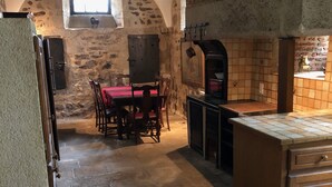 A rustic kitchen with stone walls, a wooden table with chairs, and a brick oven. - Authentic 13th century chateau, in 3 acres  surrounded by high stone walls. (Limoges)