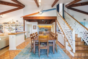 Ein geräumiger Essbereich mit Holztisch und Stühlen, im Hintergrund eine Küche und eine Treppe mit dekorativer Geländer.