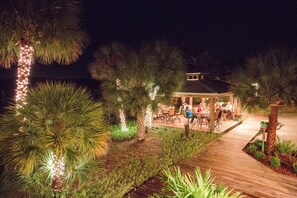 A patio area with outdoor seating, surrounded by palm trees and illuminated by string lights.