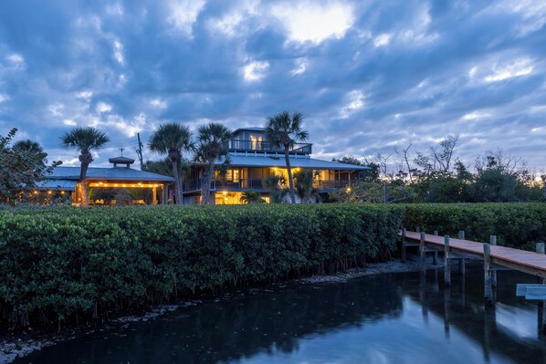 A waterfront property with a large house featuring multiple levels, a dock, and a well-maintained hedge.